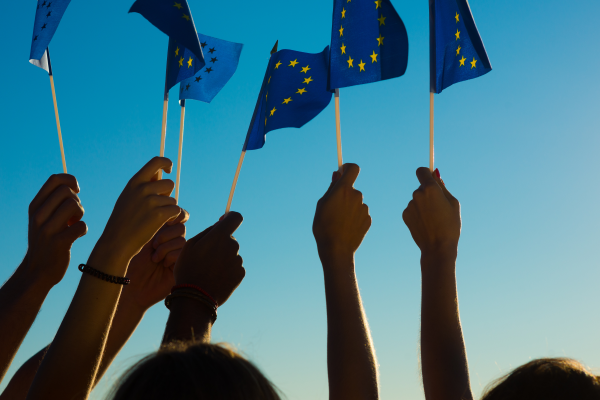 Raised hands holding European Union flags aloft, silhouetted against a vivid blue sky, symbolizing unity and European pride