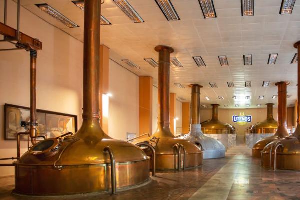 This image captures the grand interior of the Švyturys-Utenos alus brewery, showcasing a vast array of large tanks.